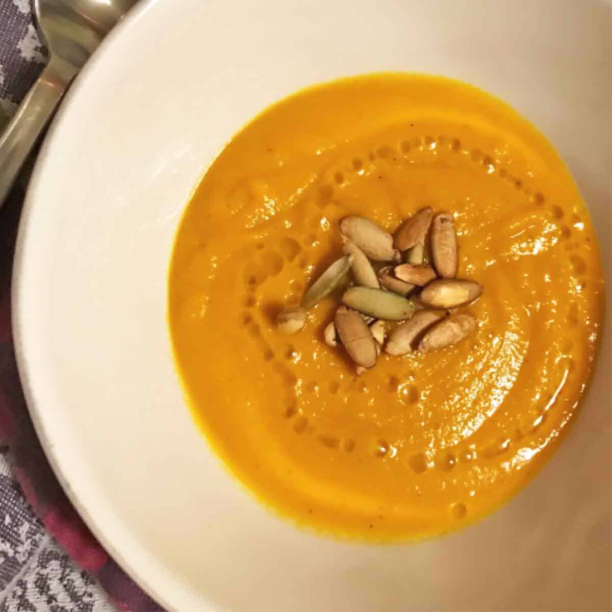 Carrot soup in a bowl topped with pumpkin seeds and drizzled with olive oil.