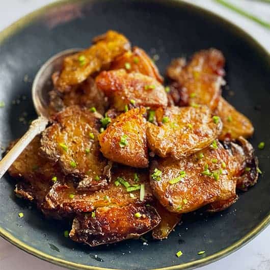 Crispy Smashed Potatoes in a black bowl with a serving spoon.