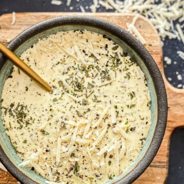 Caesar dressing in a bowl topped with parmesan cheese and dried herbs.