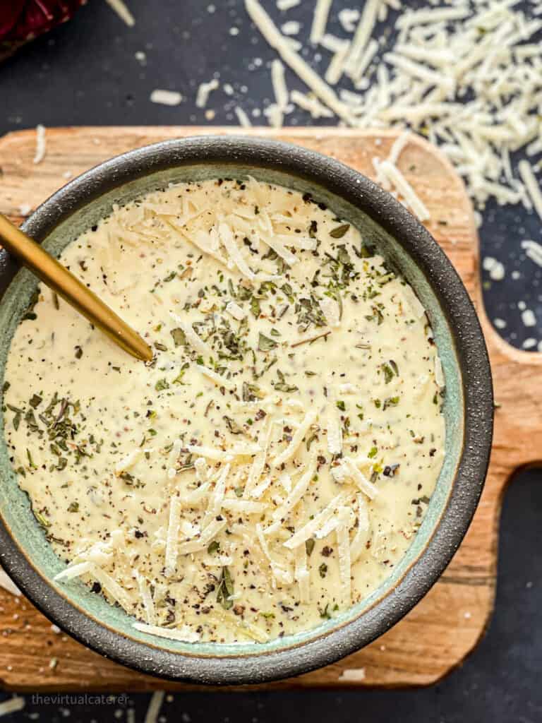 Caesar dressing in a bowl topped with parmesan cheese and dried herbs.