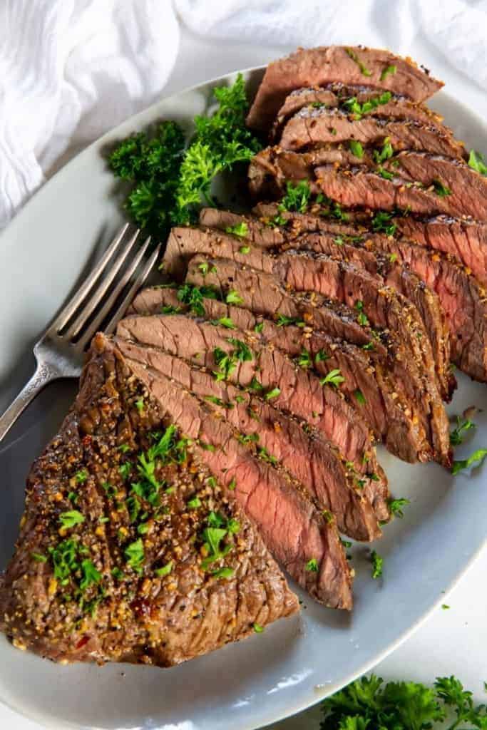 London Broil sliced on a white plate with parsley garnish and a fork