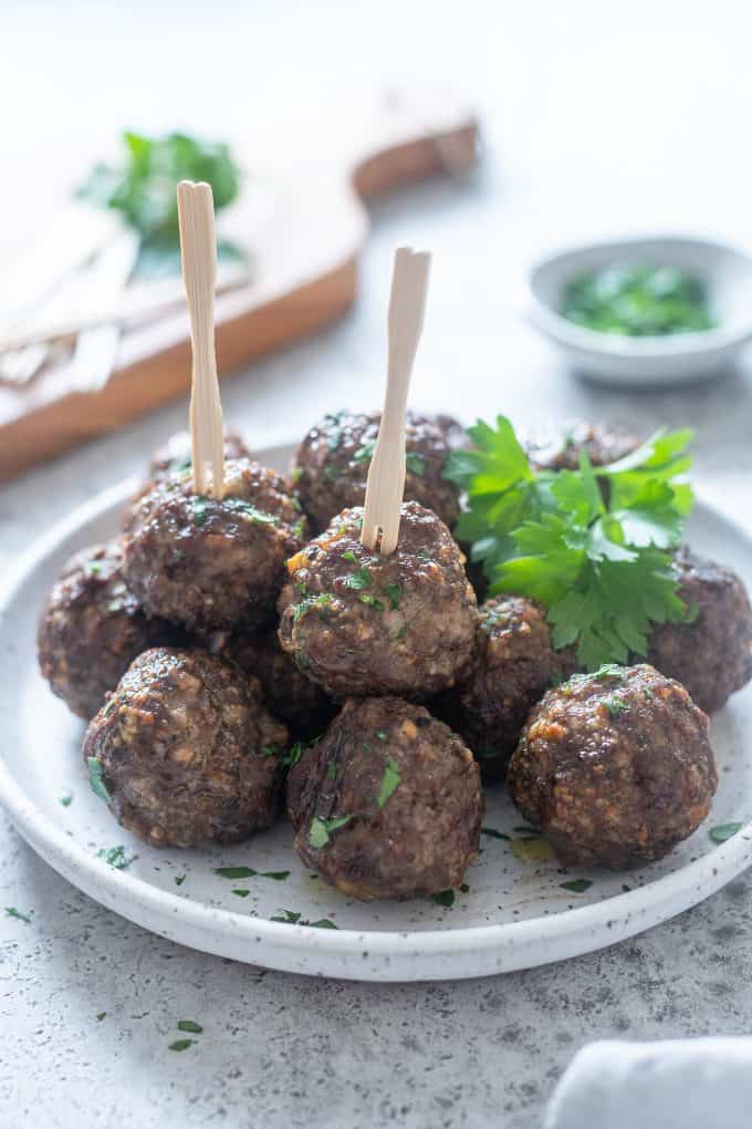 Meatballs on a white plate with toothpicks and a parsley garnish