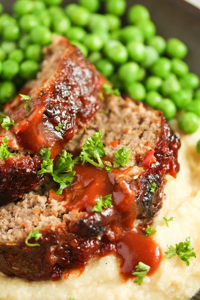 Close-up of meatloaf with ketchup garnished with parsley and served with peas