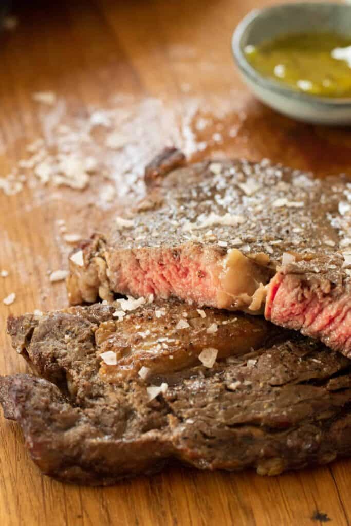 Ribeye steak cut on a wood cutting board topped with flaky sea salt