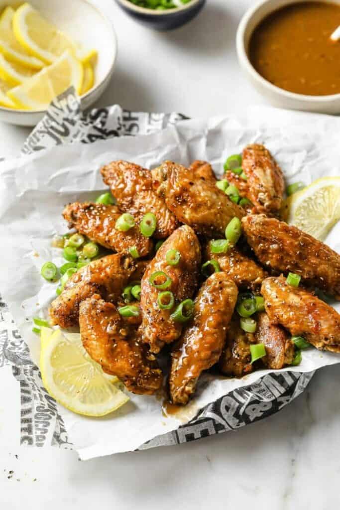 crispy-air-fryer-lemon-pepper-chicken-wings- in a basket with paper topped with green onions and a side of lemon