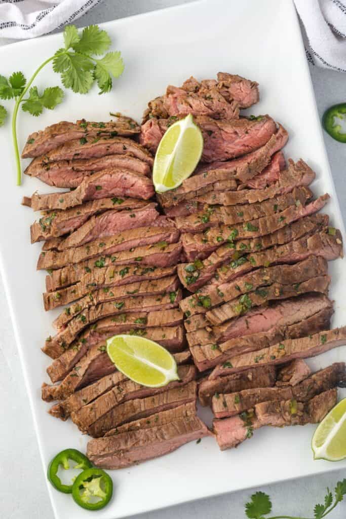 Sliced flank steak on a plate with lime and cilantro garnish