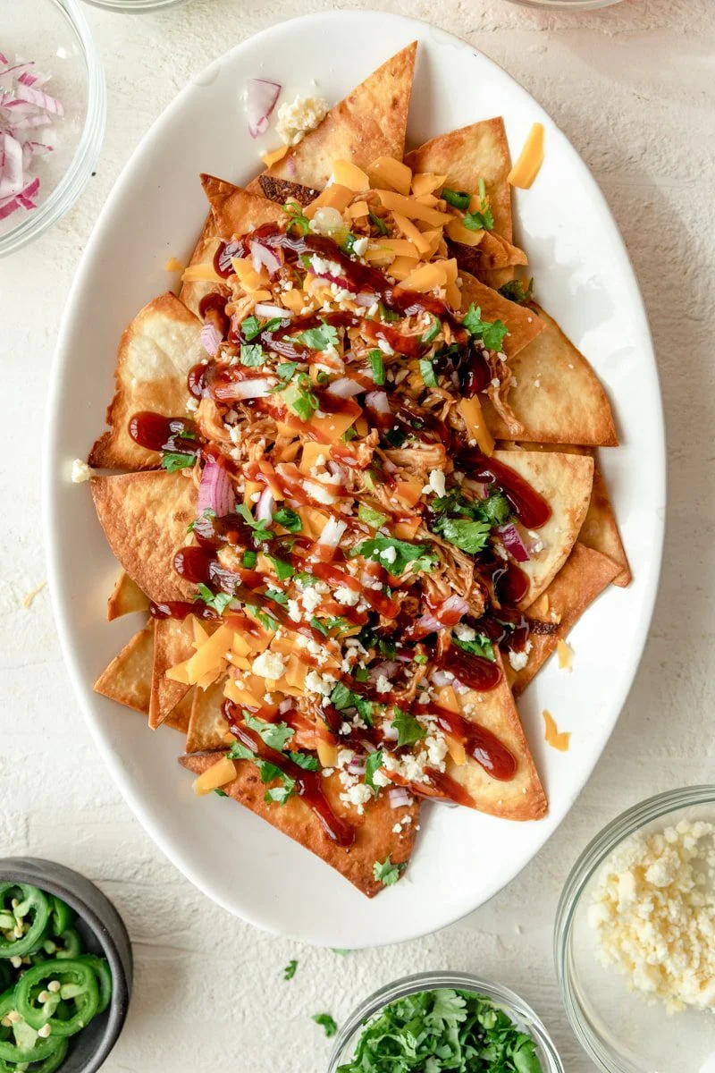 Nachos on an oval plate topped with cheese and herbs.