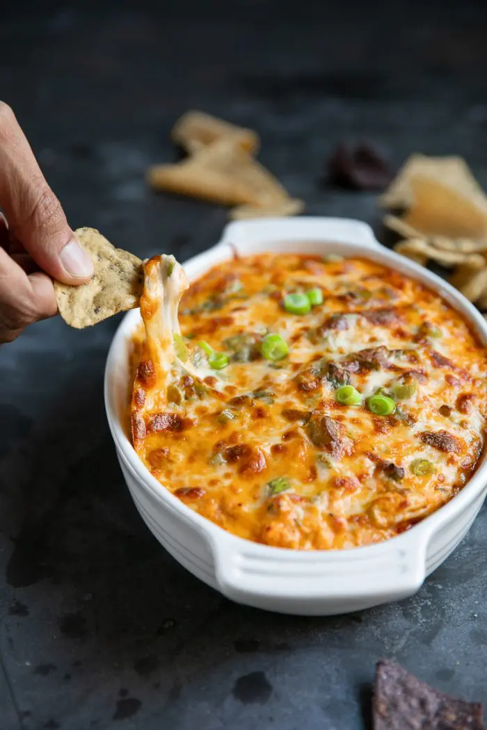 Hot dish filled with cheesy dip.  Hand holding a chip and scooping the dip to eat.