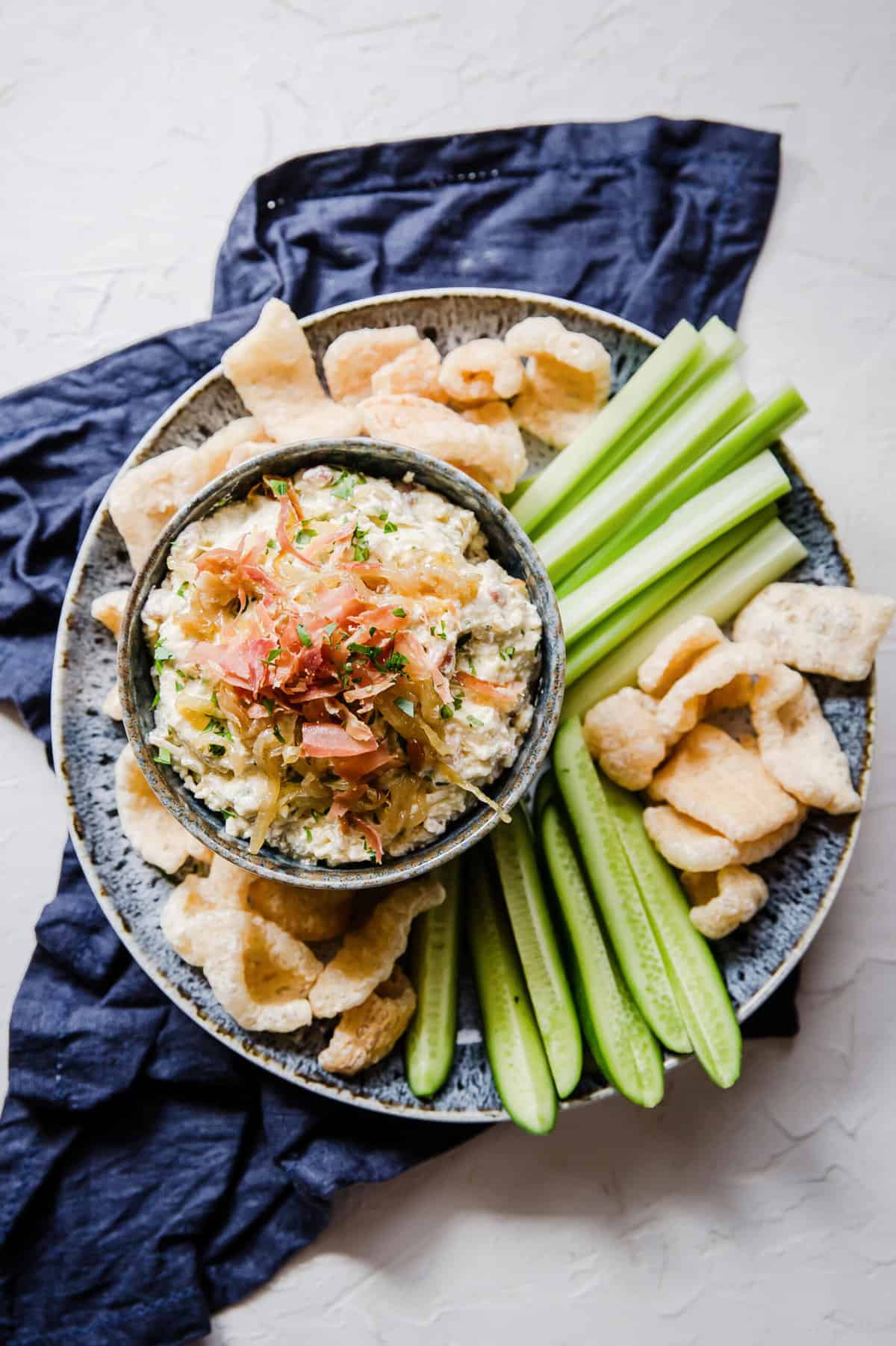 Bowl full of dip surrounded by veggies on a larger plate.