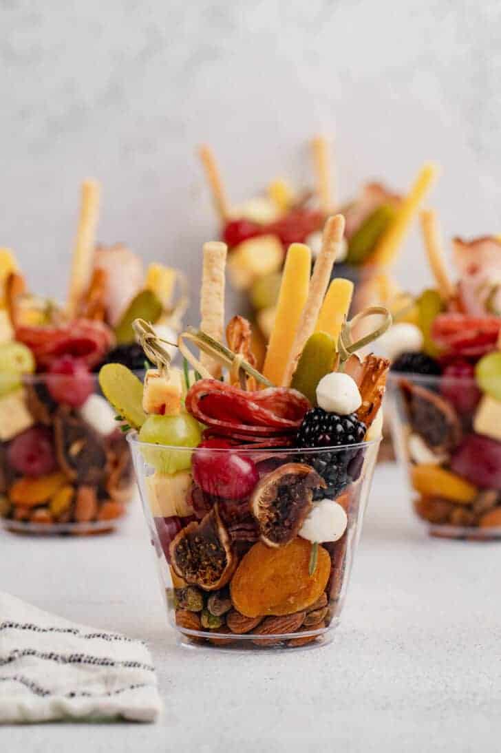 Cups filled with meats, fruit, cheese and breadsticks. 