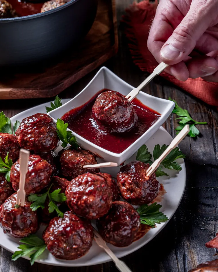 Meatballs on a plate.  One is dipped into a square bowl of sauce.
