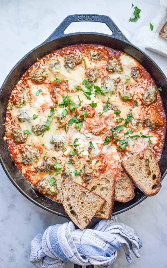 Skillet filled with meatballs and dip and garnished with crostini bread.