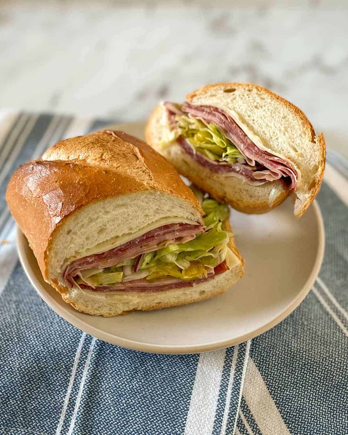 Sandwich on a plate, sliced in half with meats showing.