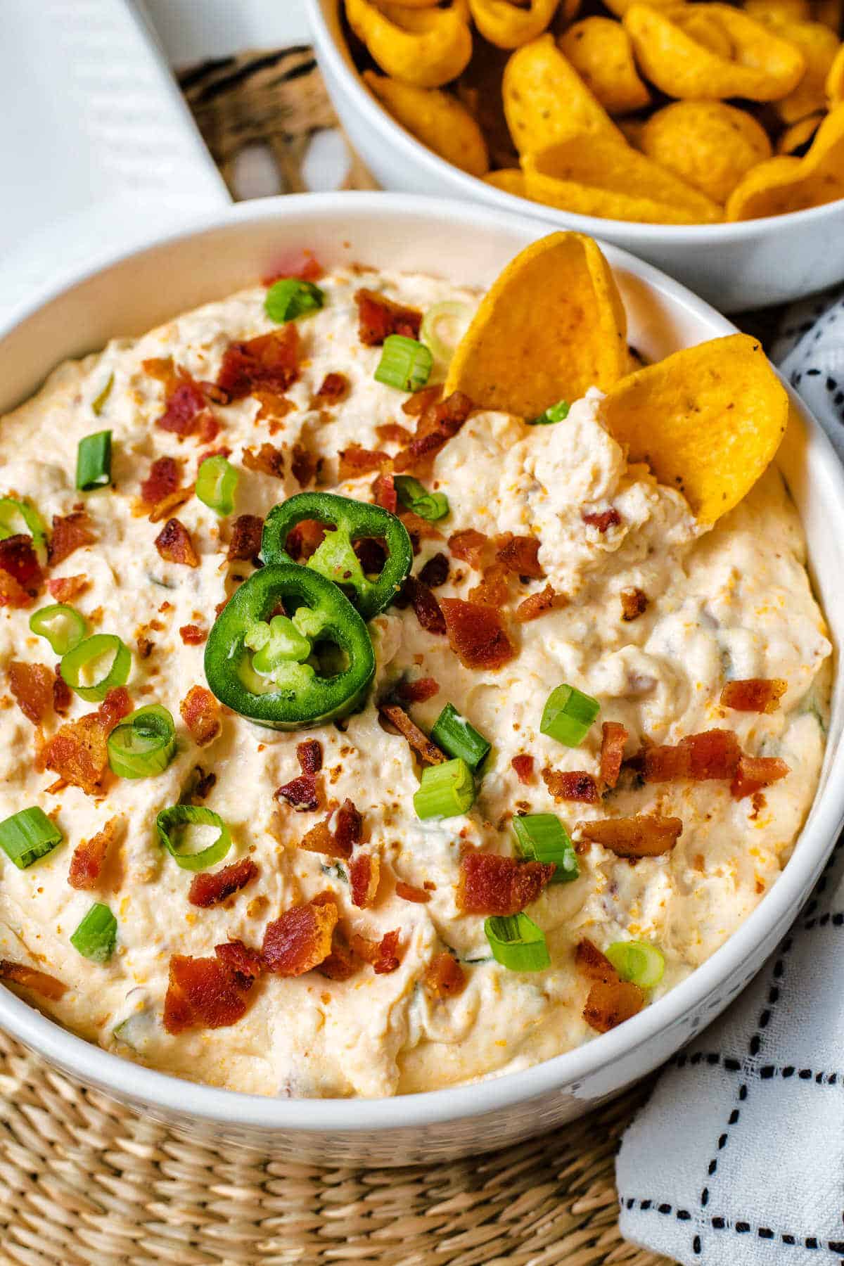 Bowl full of dip with jalapenos, bacon and chips.