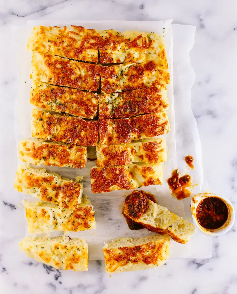 Garlic bread fingers served on a marble slab with a side of tomato dipping sauce.