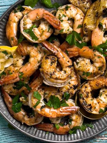 Cooked Shrimp on a metal plate with a spoon holding a shrimp. Shrimp topped with parsley and lemon.
