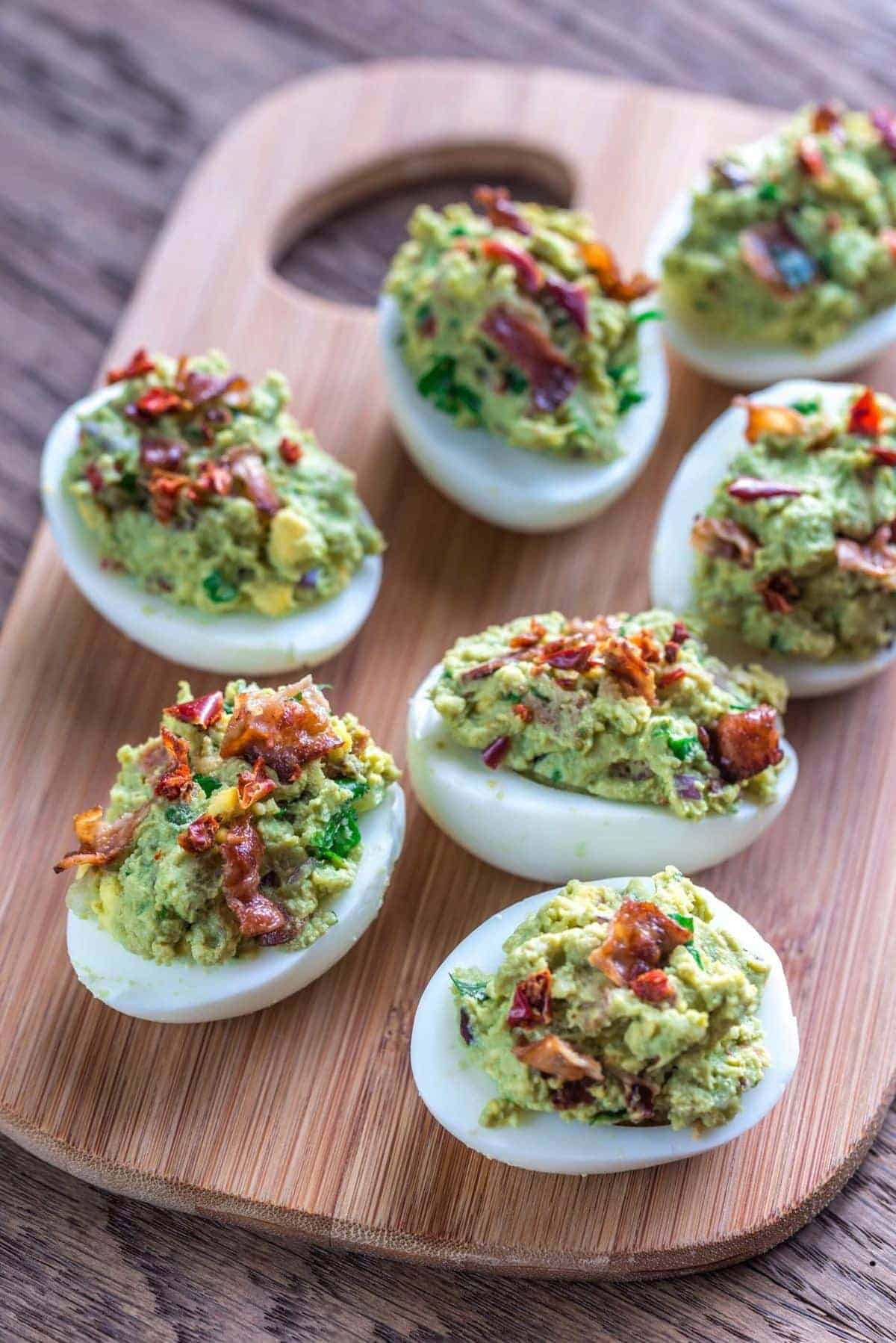 Deviled eggs on cutting board stuffed with bacon and guacamole.