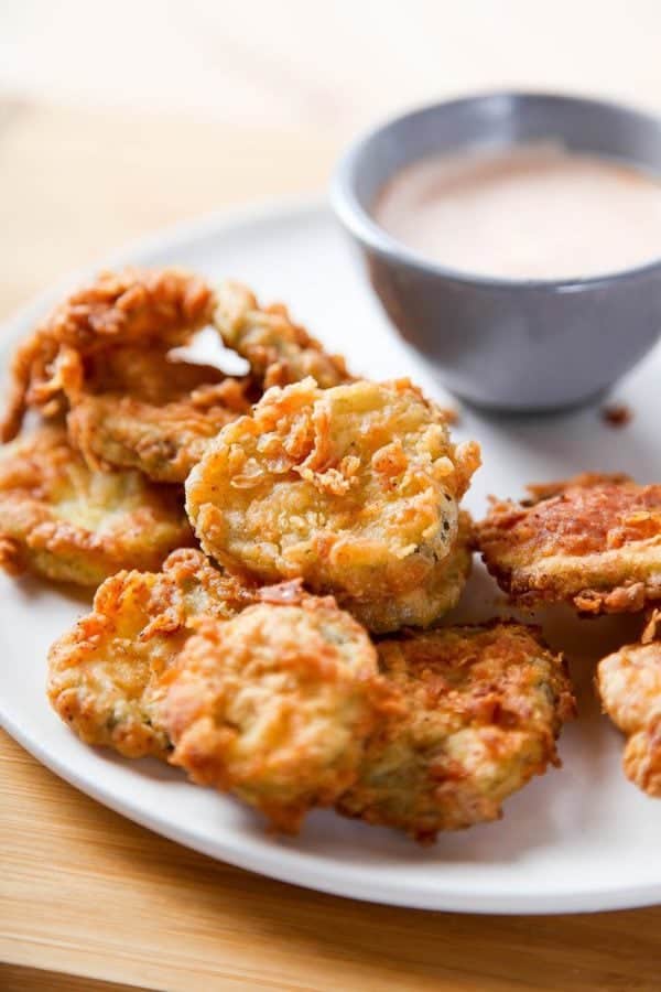 Deep fried pickles on a plate with a bowl of dipping sauce on the side.