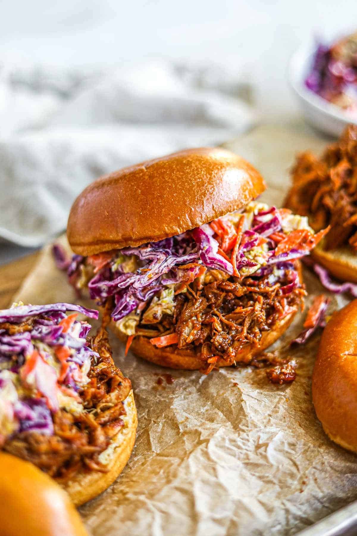 Sliders on tan crinkled parchment paper with shredded chicken and slaw.