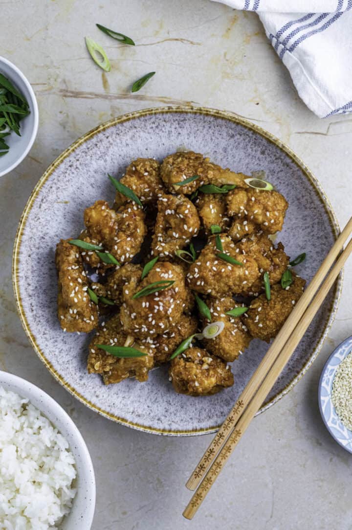 crispy cauliflower wings on a speckled round plate.  Served with chopsticks.