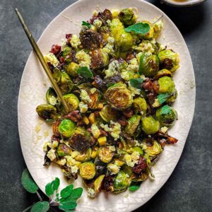 An oval plate of roasted Brussels sprouts with sausage and served with a spoon.