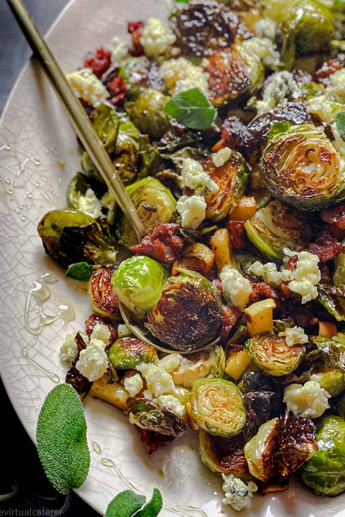 Sheet Pan Brussels sprouts on a plate with sausage, blue cheese, apples and sage. Served with a gold spoon.