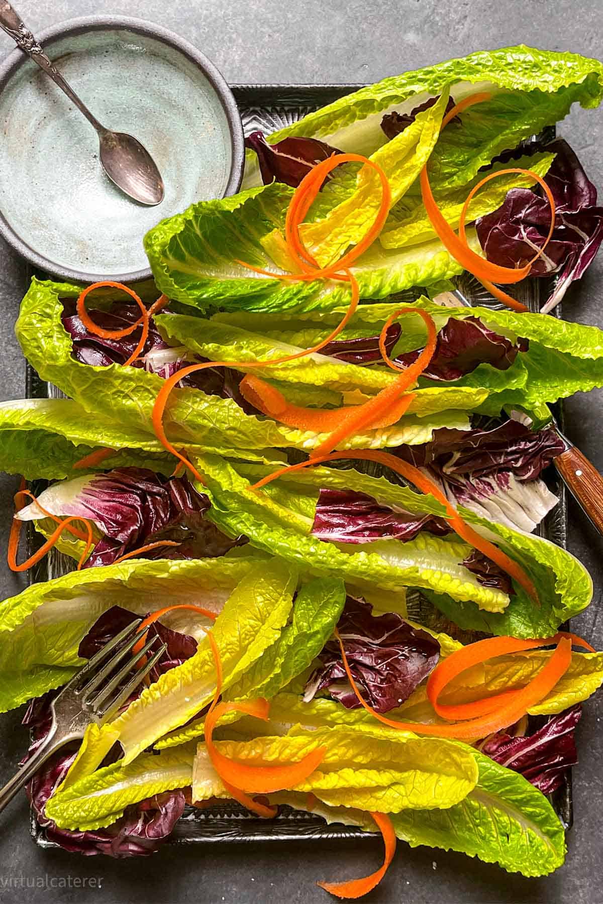Leaves of romaine and radicchio on a sheet pan with strips of carrots.
