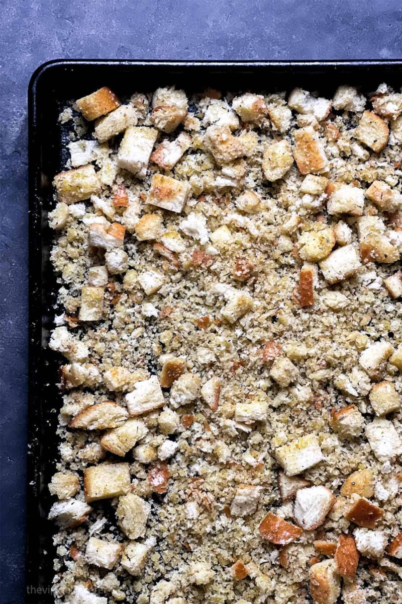 A sheet pan full of a mixture of croutons and breadcrumbs ready to be baked.