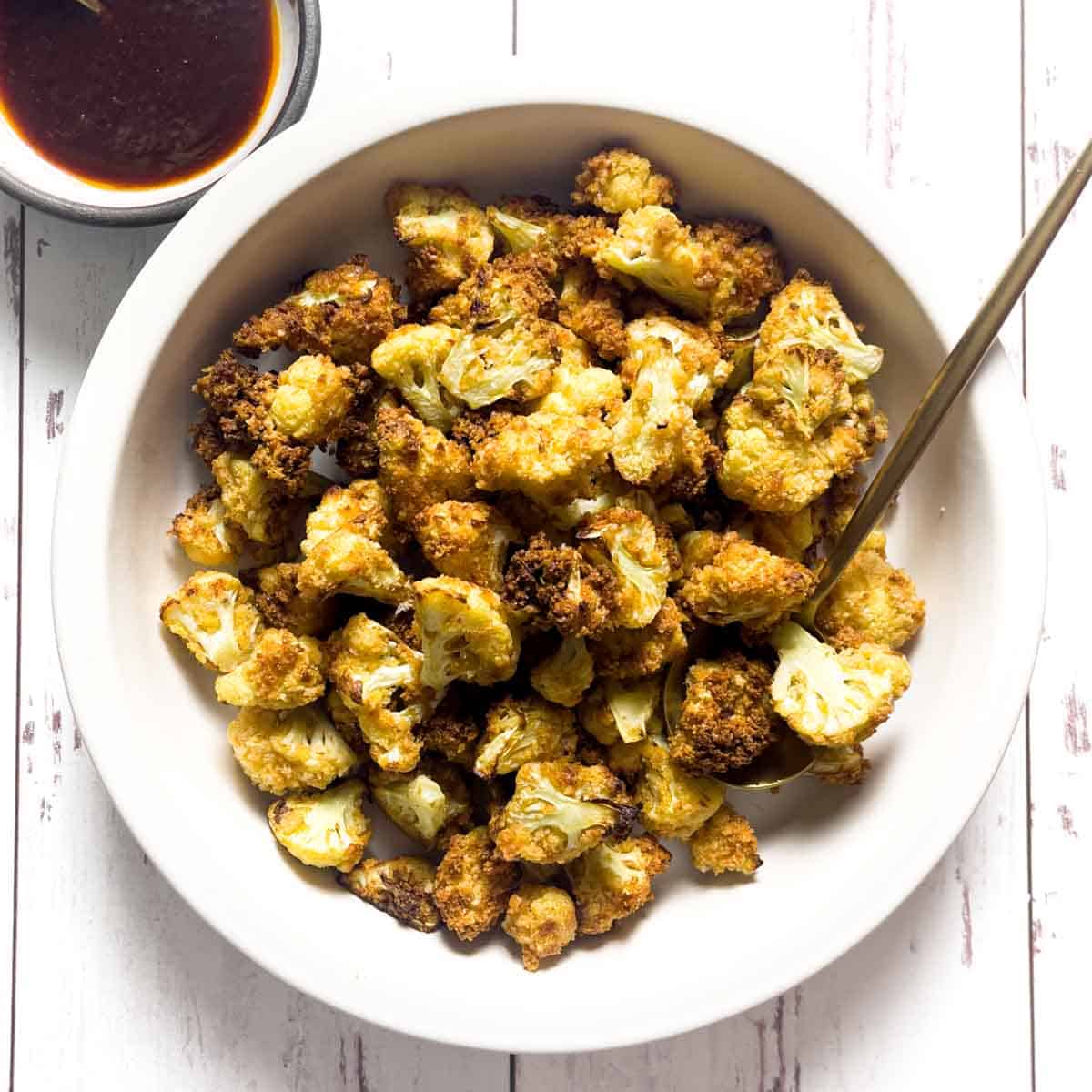 Cauliflower Bites in a white bowl, served with a gold spoon and a side of honey chipotle sauce.