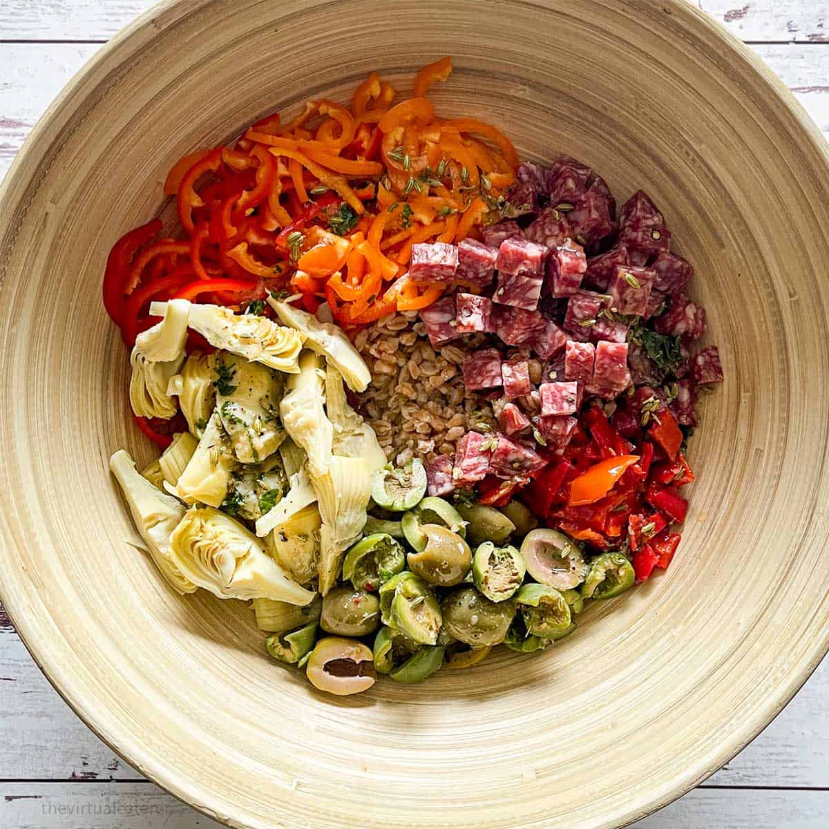 Bamboo bowl filled with farro, vegetables, olives and salami.