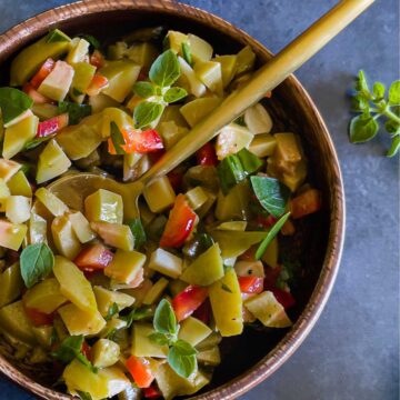 A wood bowl filled with chopped olives and veggies on a blue background with a gold serving spoon.