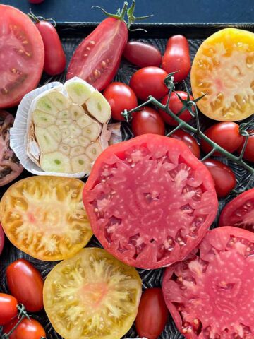 A sheet pan filled with a variety of fresh tomatoes. Some are whole and some are cut in half.