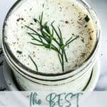 A jar of dressing topped with herbs.