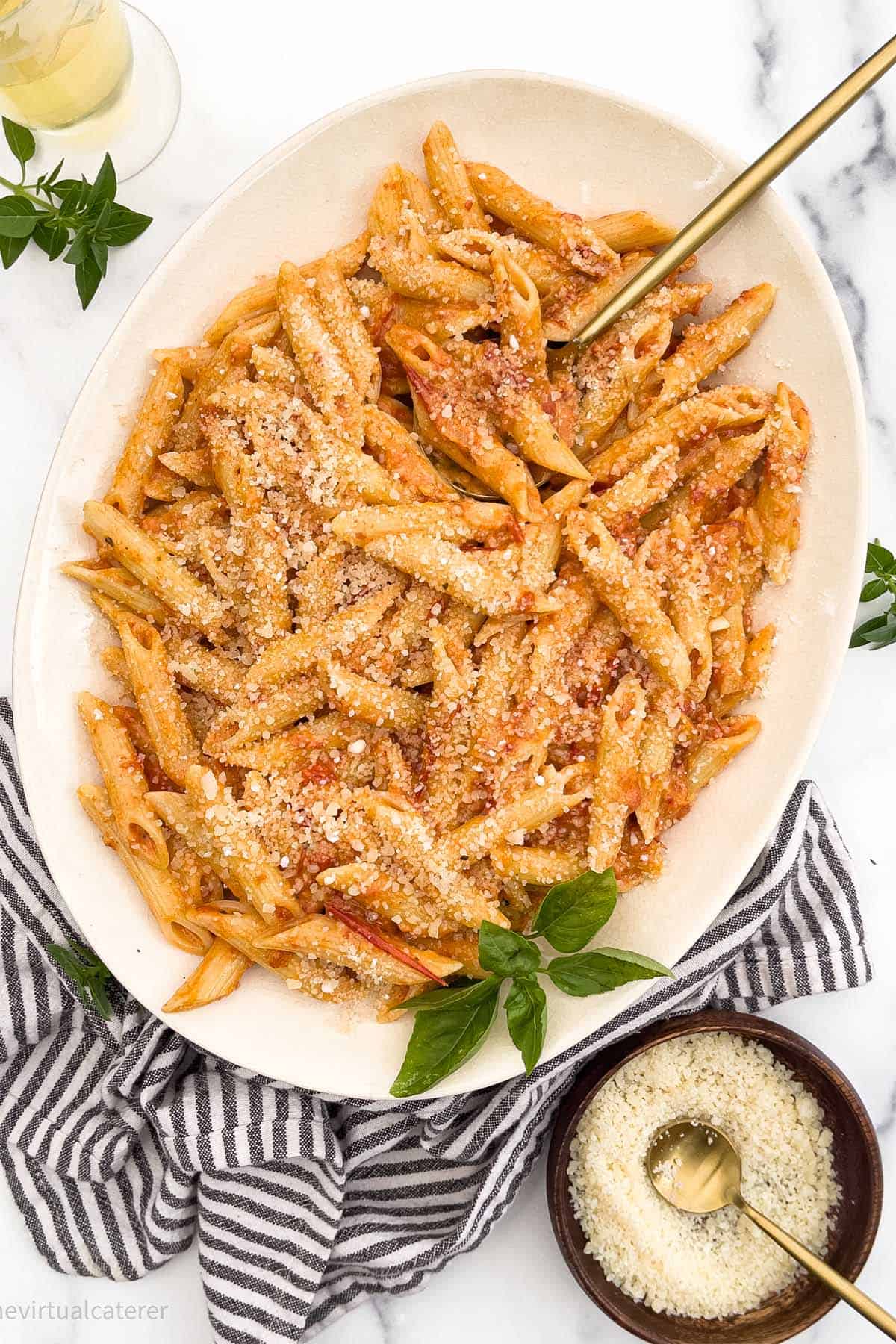 A plate of penne pasta with blush sauce.  Served on a white plate with wine and parmesan cheese.