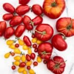 A group of different types of tomatoes on a white marble background.