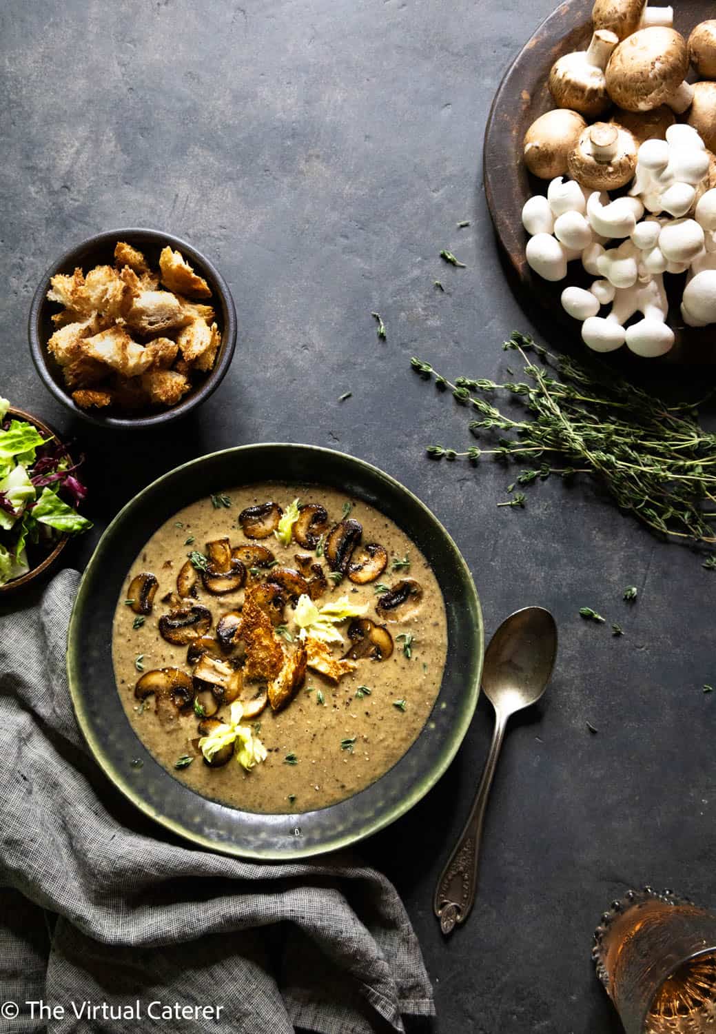 Soup in a green bowl with sauteed mushrooms, croutons, and thyme on a dark background.