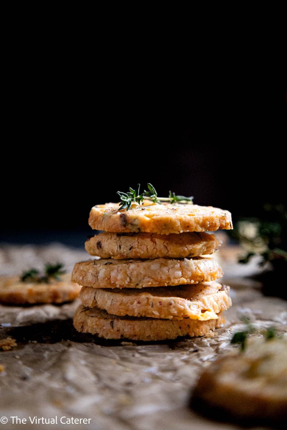 A stack of cookies topped with fresh thyme on parchment paper.