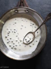 A saute pan of caper cream sauce with a spoon.
