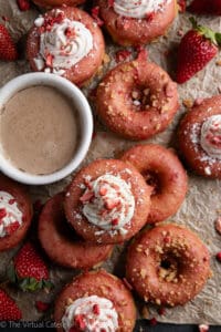 Strawberry cheesecake donuts served with coffee on crumpled parchment paper.