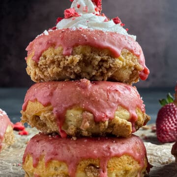 A stack of donuts on with pink icing running down the sides on parchment paper. Topped with cream cheese frosting and dried strawberries from the side view.