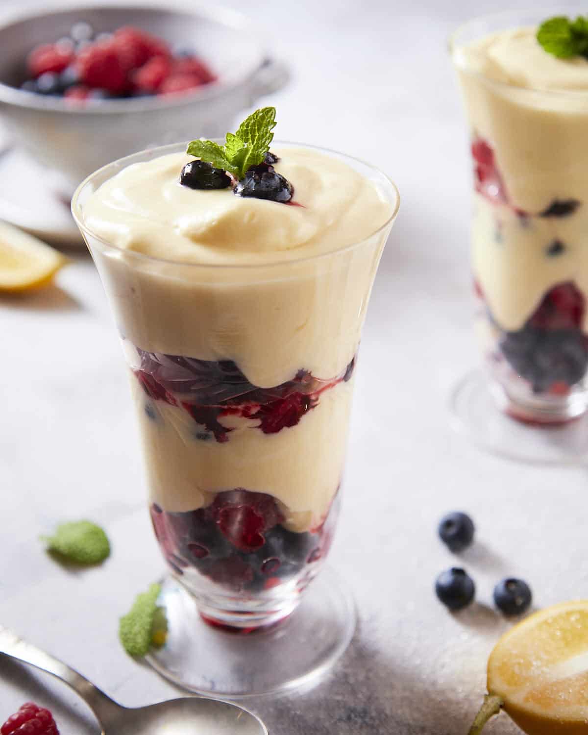 A parfait glass filled with mixed berries and lemon cream served with fresh mint and a spoon.