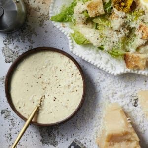 Caesar dressing with mayo on the side of a Caesar salad with parmesan cheese and black pepper.