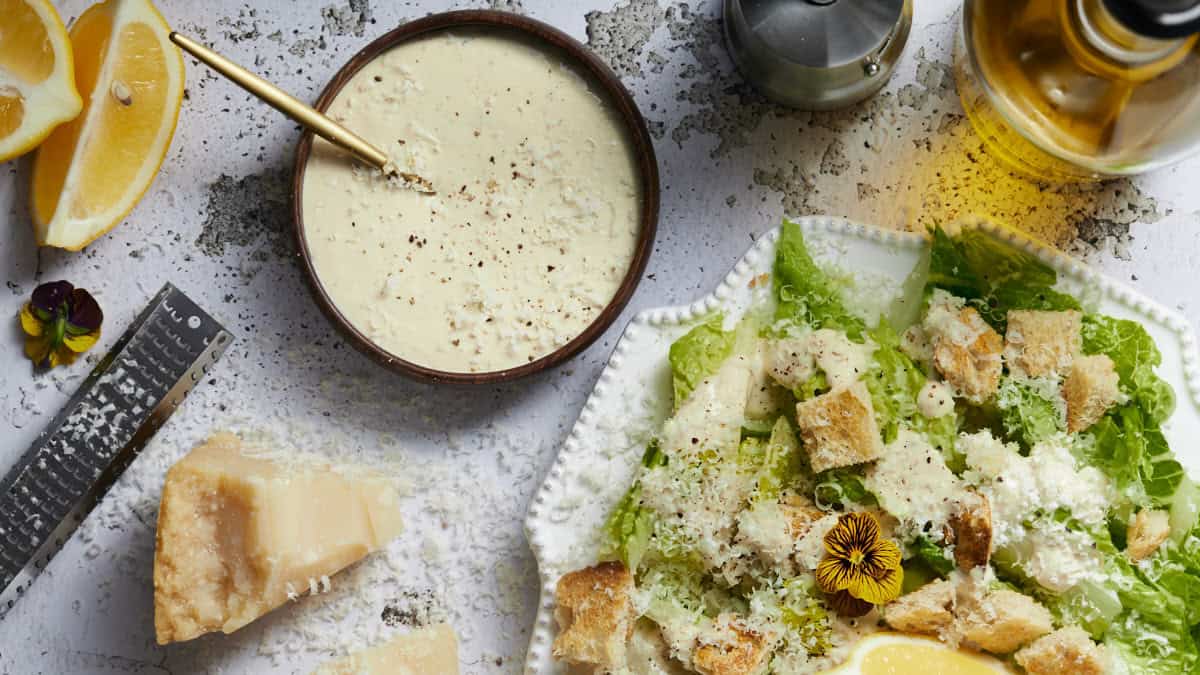  A side of Caesar dressing with a Caesar salad and parmesan cheese.
