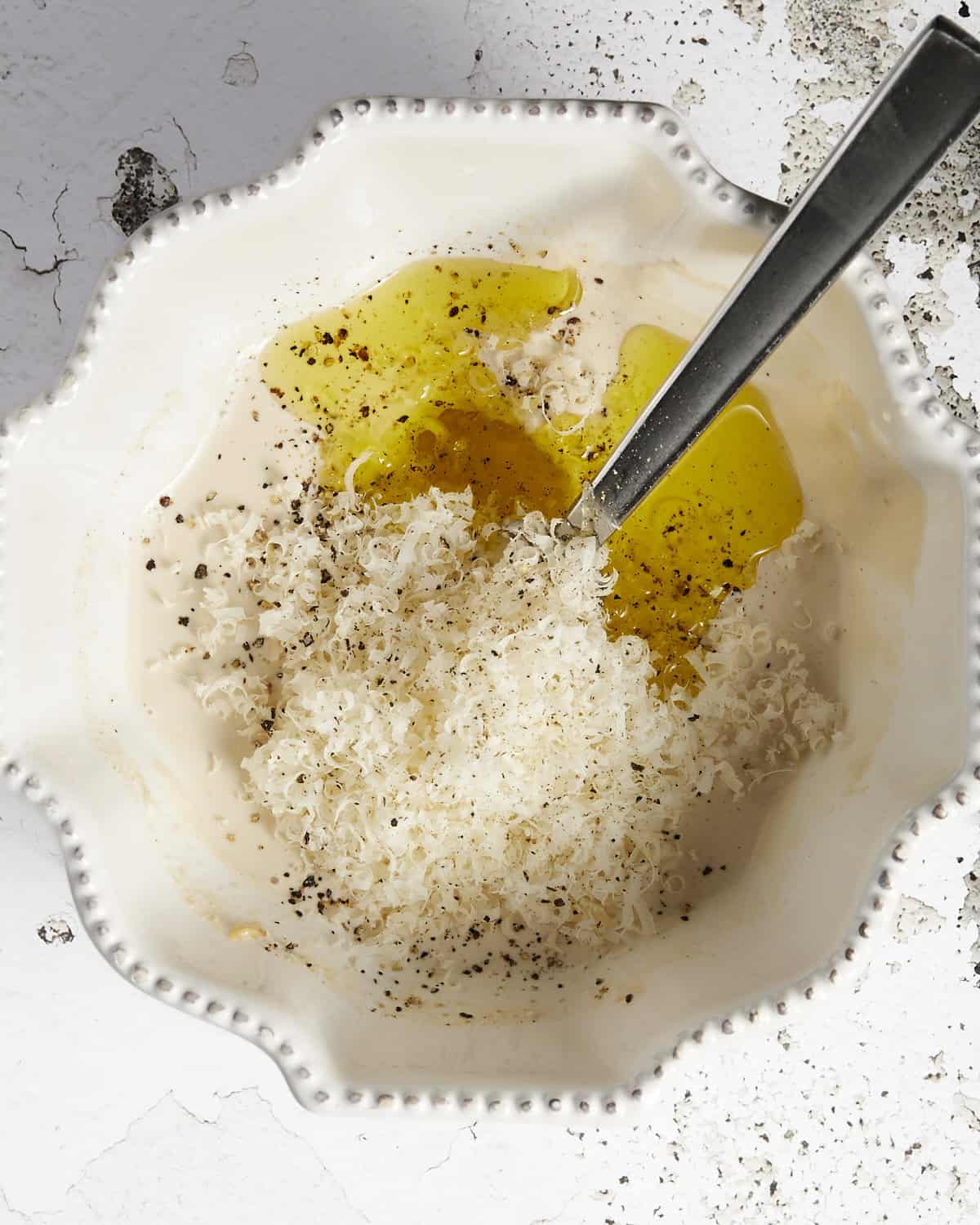 Caesar dressing with mayo in a bowl with parmesan cheese and olive oil before it's mixed.