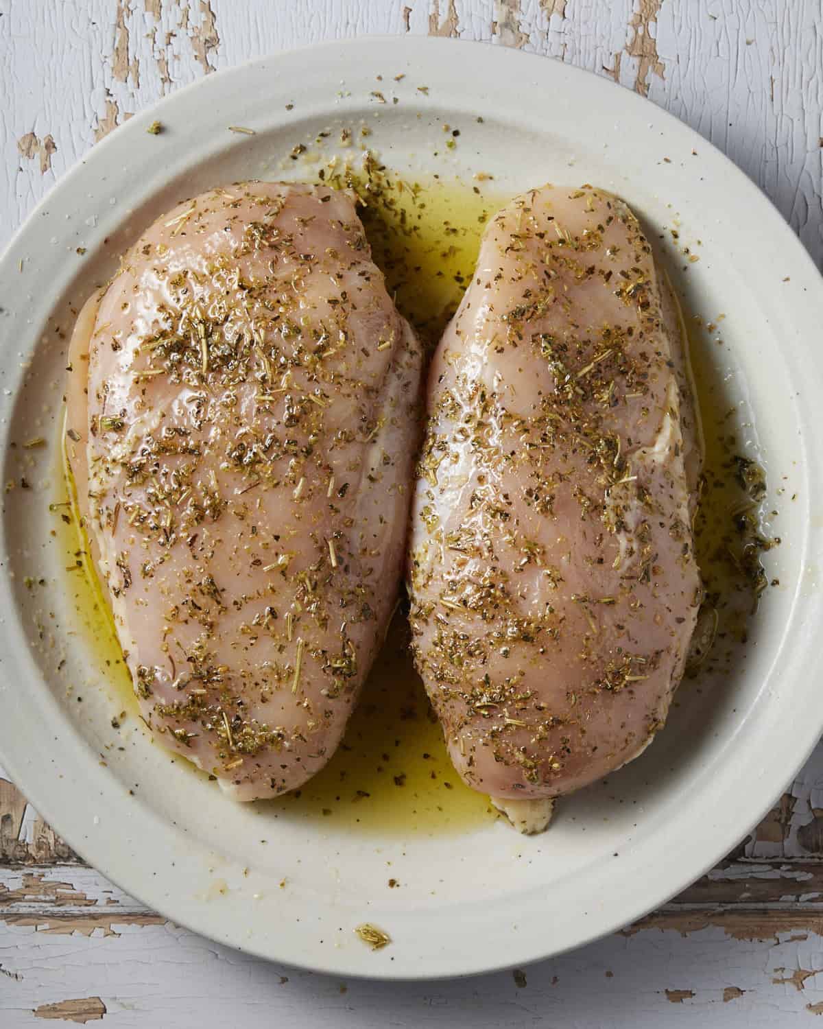 Raw chicken breasts marinated in olive oil, salt, pepper and Italian seasoning. 