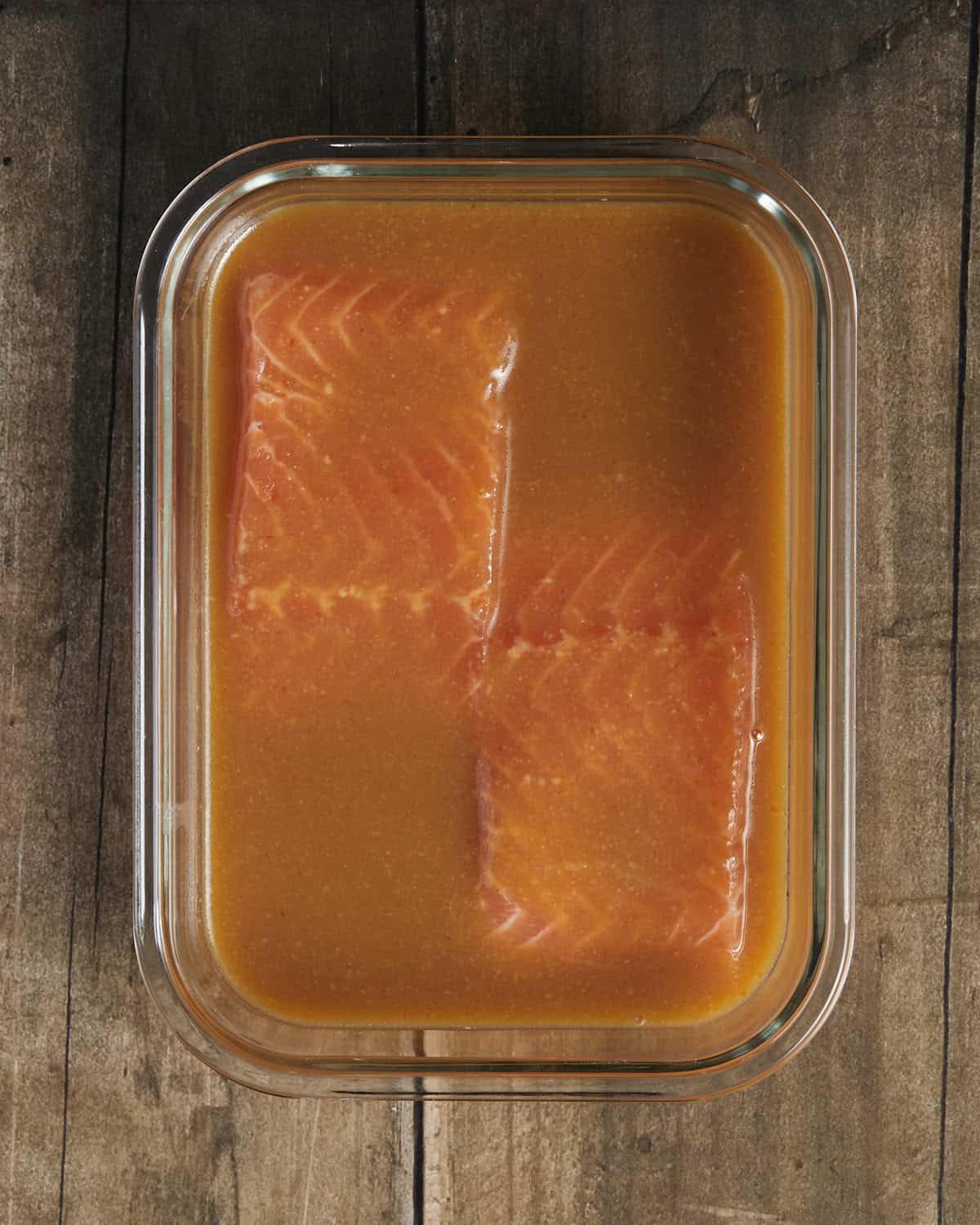 Salmon filets marinating in a glass container with honey miso marinade over them. 