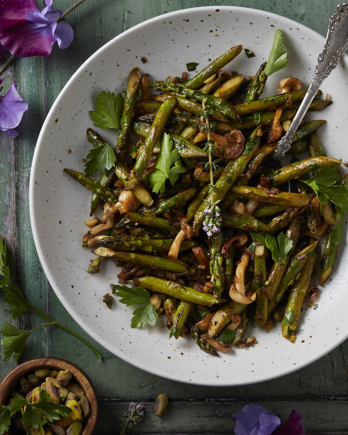 A plate of sauteed asparagus with mushrooms served with a spoon. 