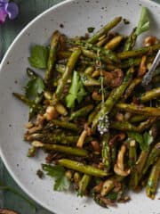 A white plate holding sauteed asparagus with mushrooms and finished with fresh herbs.