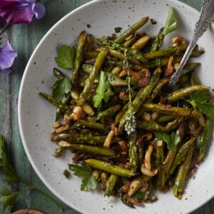 A white plate holding sauteed asparagus with mushrooms and finished with fresh herbs.
