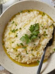 Easy oven-baked risotto in a bowl with parsley lemon and olive oil garnishes.